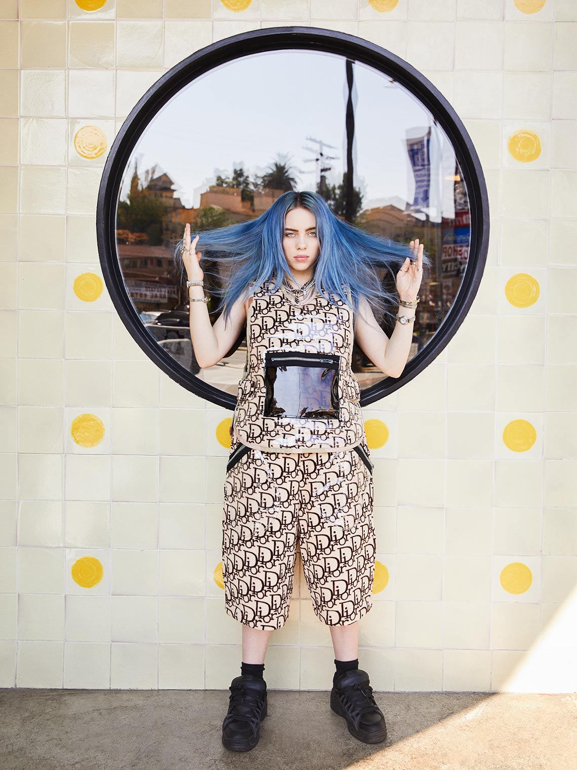 Billie Eilish standing with pulling blue hair on the side. 